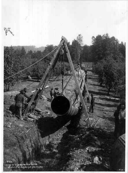 Workers laying a large-diameter steel pipeline in a trench, 1899